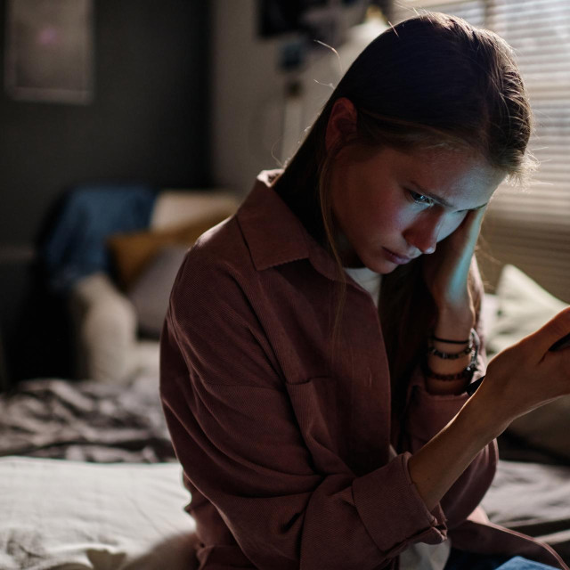 Offended girl with smartphone suffering from night and day cyberbullying