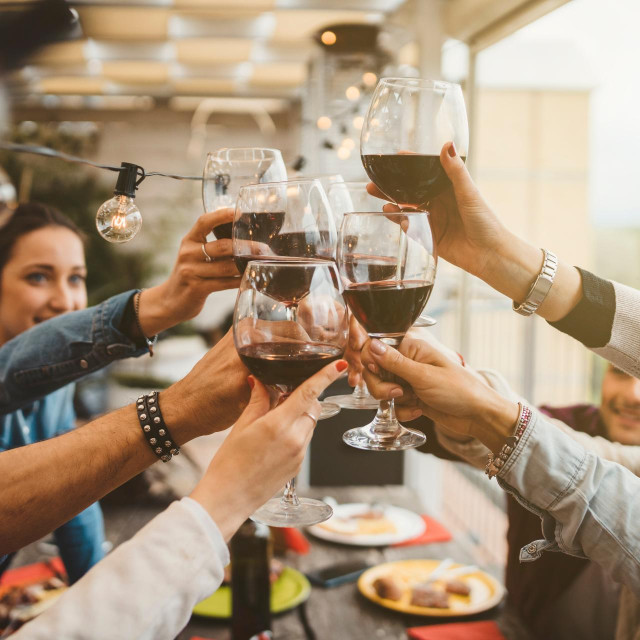 Young friends celebrating at dinner at sunset - Detail of hands while toasting with glasses of wine - Happy people at a terrace party after the harvest before sunset - Concept of friendship