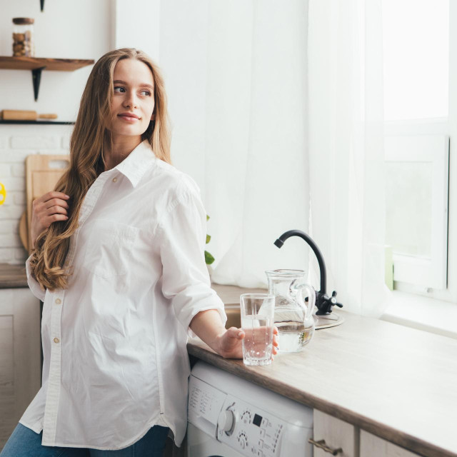 Young cute pregnant girl drinking clean water in the kitchen. The concept of a healthy lifestyle. Toning.