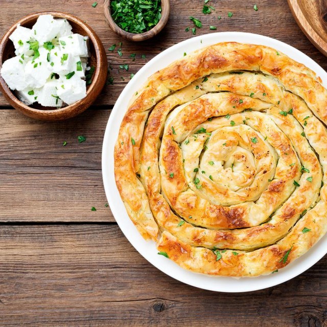 Traditional feta cheese phyllo pastry pie on wooden background.