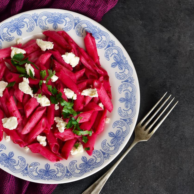 Pasta with beet sauce and feta cheese on a black background