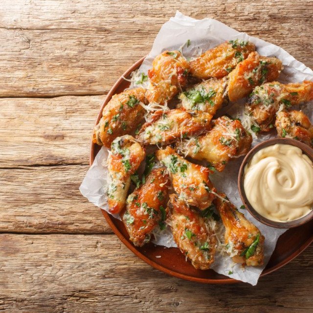 Classic Garlic Parmesan Butter Chicken Wings served with mayonnaise close-up in a plate on the table. Horizontal top view from above