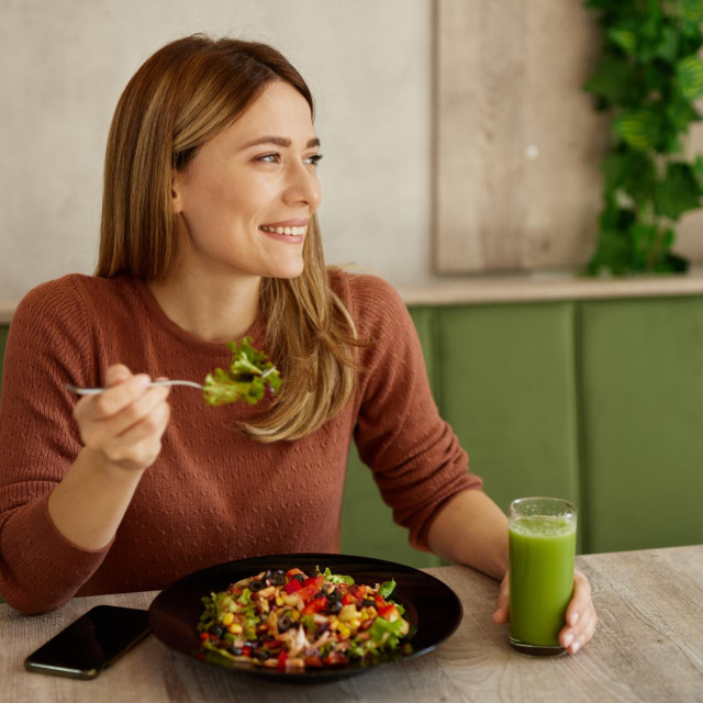 Mid adult woman enjoys eating salad and drinking smoothie in salad bar